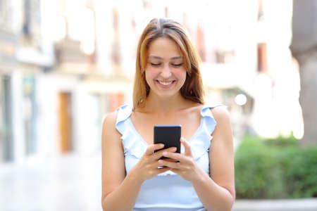 Front view portrait of a happy female walking using smartphone in the streetの写真素材