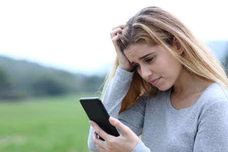 Worried teenage girl complaining checking smart phone message outdoors in the mountainの写真素材
