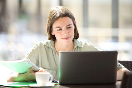 Satisfied student e learning with laptop and notes in a coffee shopの写真素材