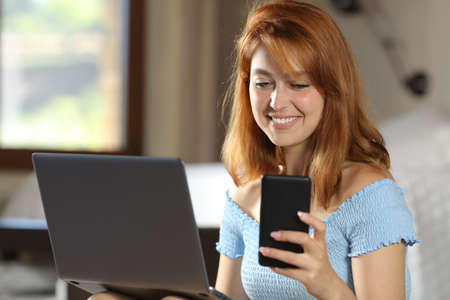 Happy woman using laptop and mobile phone in a house roomの写真素材
