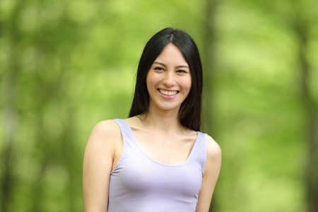 Front view portrait of a happy asian woman smiling looking at camera in a green parkの写真素材