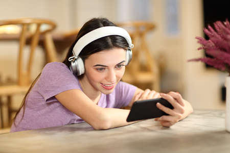 Happy woman at home wearing headphones watching videos on smart phoneの写真素材
