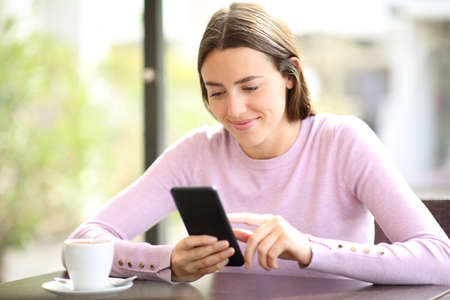 Happy woman relaxing in a coffee shop using mobile phoneの写真素材