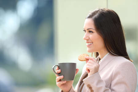 Happy businesswoman eating cockie and drinking coffee outdoors in the streetの写真素材