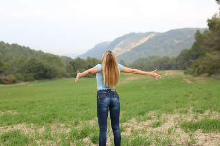 Back view portrait of a happy teen outstretching arms in a fieldの写真素材