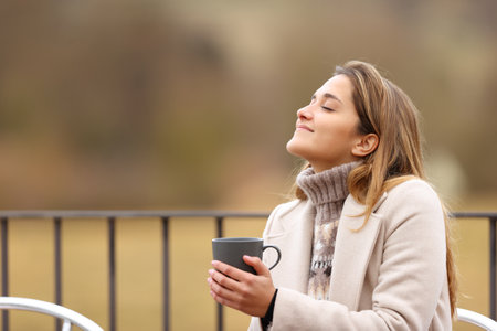 Happy woman holding coffee mug and breathing fresh air in winter in a terraceの写真素材