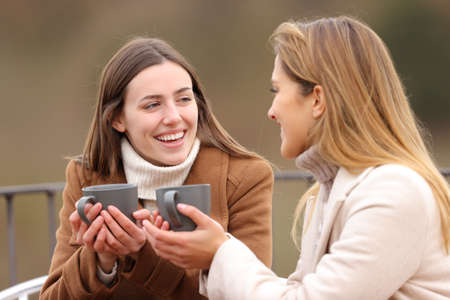 Two happy friends drinking and talking in winter in a terraceの写真素材