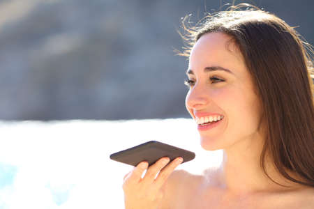 Happy woman using voice recognition on smart phone on the beachの写真素材