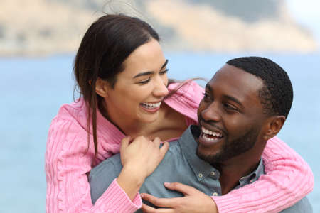 Happy couple joking and laughing on piggiback on the beach