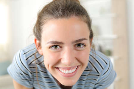Front view portrait of a happy woman looking at camera with white smile joking at homeの写真素材