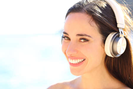 Portrait of a happy woman with wireless headphones listening to music on the beachの写真素材