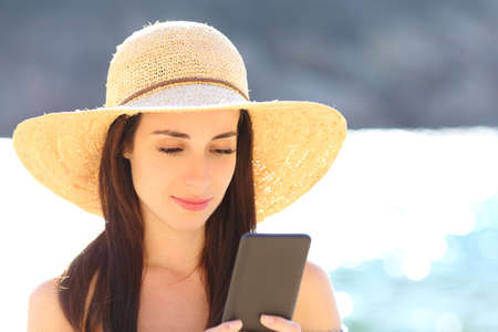 Serious woman using smart phone walking on the beachの写真素材