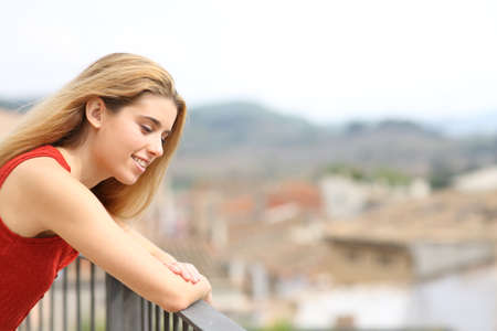 Happy woman looking down smiling in a balcony in a rural townの写真素材
