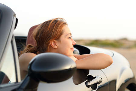 Satisfied woman contemplating views resting from a convertible car