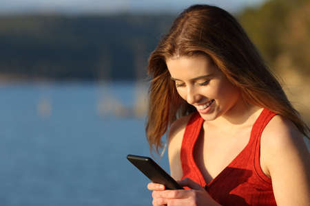 Happy woman in red using smart phone in a lake at sunsetの写真素材