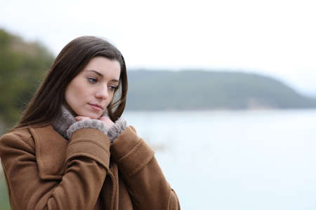 Pensive woman in winter thinking in a lake looking downの写真素材