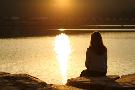 Back view of a woman silhouette contemplating sunset in a lakeの写真素材