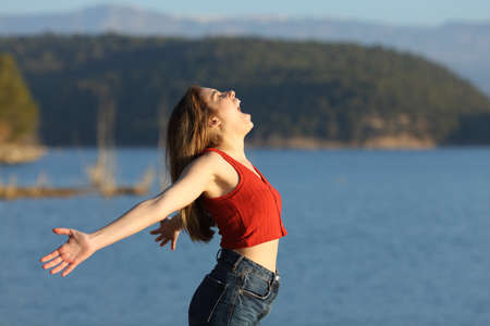 Excited woman in red screaming to the air outstretching arms in a lake on a sunny dayの写真素材
