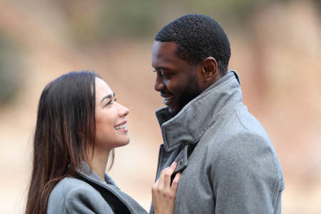 Happy interracial couple in love flirting looking each other in winter