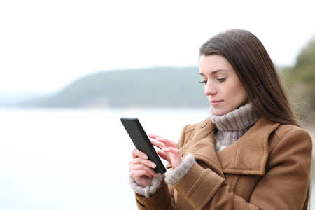 Serious woman using mobile phone in winter in a lakeの写真素材