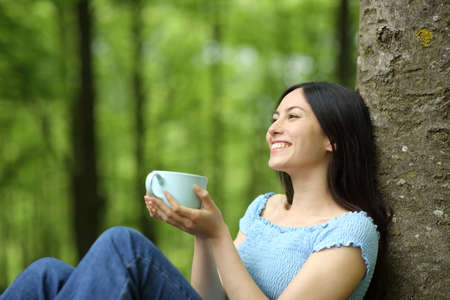 Happy asian woman relaxing drinking coffee sitting in a parkの写真素材