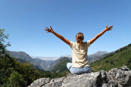 Back view portrait of a happy woman celebrating vacation sitting in nature contemplating viewsの写真素材