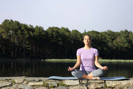Front view portrait of a woman doing yoga lotus pose in the mountainの写真素材