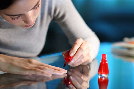 Close up of a woman painting nails in red in the night at homeの写真素材