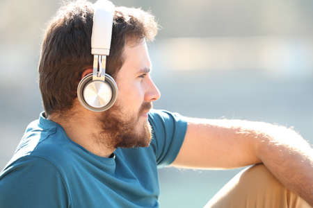 Man wearing headphones relaxing and looking away listening to music outdoors