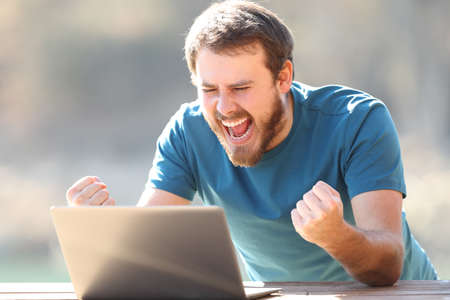 Excited man checking laptop content celebrating good news outdoorsの写真素材