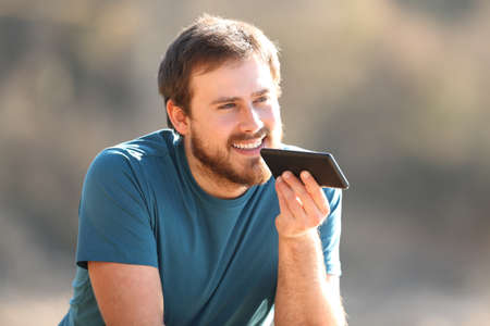 Happy man using voice recognition on cellphone contemplating outdoors