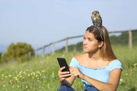 Woman using smartphone disgusted with an owlet on head sitting in a meadowの写真素材