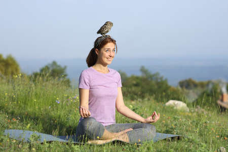 Happy woman doing yoga in a meadow distracted with a bird on headの写真素材