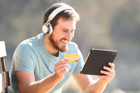 Happy man with headphones buying music or videos with a tablet and credit card onlineの写真素材