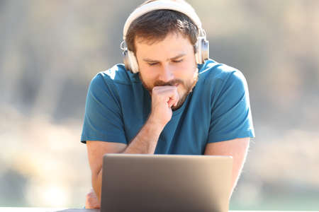 Front view portrait of a man wearing wireless headphones listening and watching videos on laptop...