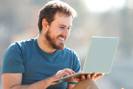 Happy man using laptop watching media content sitting in natureの写真素材