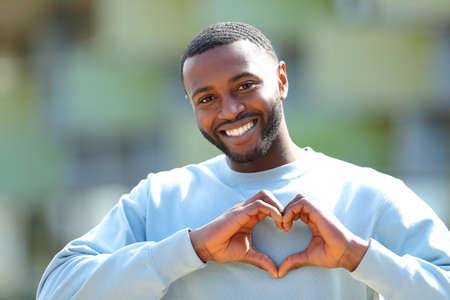 Front view portrait of a happy man with black skin doing heart shape outdoorsの写真素材