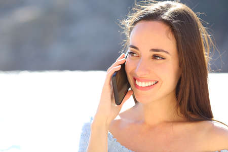Happy woman talking on mobile phone walking on the beach on summer vacationの写真素材