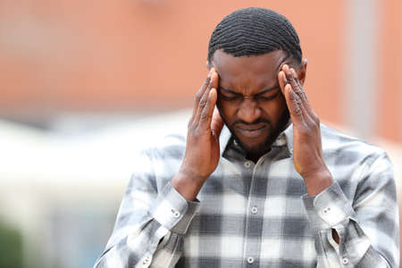 Front view portrait of a man with black skin suffering migraine in the street