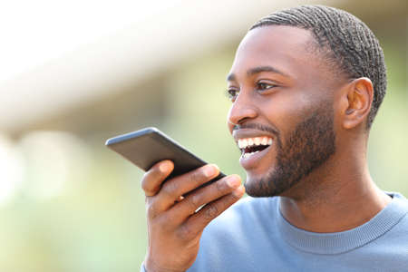 Happy man with black skin dictating text on cell phone in the streetの写真素材