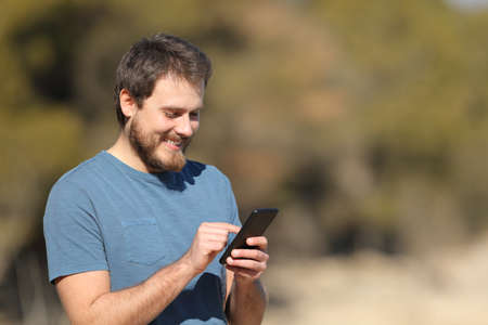 Happy man checking cellphone standing in natureの写真素材