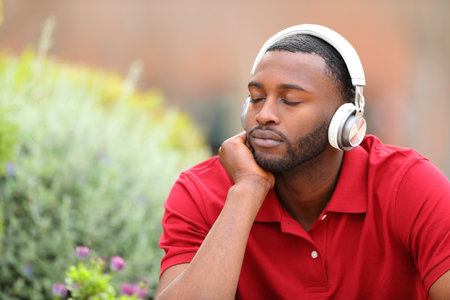 Man with black skin resting with closed eyes listening to music from wireless headphones in a parkの写真素材