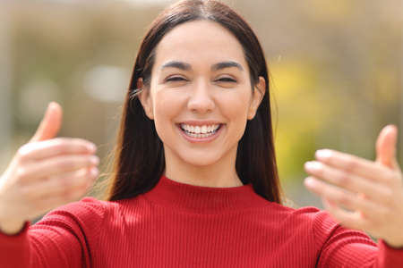 Front view of a happy woman in red saying come with me gesturing with both hands in a park