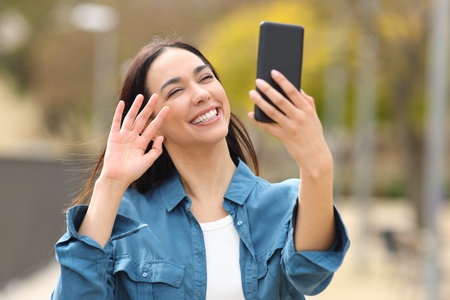 Happy woman greeting having videocall or taking slefie on phone in a parkの写真素材