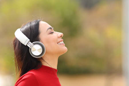 Side view portrait of a happy woman listening to music wearing wireless headphones in a parkの写真素材