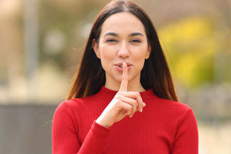 Front view of a happy woman in red asking for silence with finger on lips in the streetの写真素材