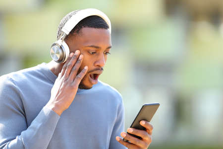 Shocked man with wireless headphones and smart phone in the streetの写真素材