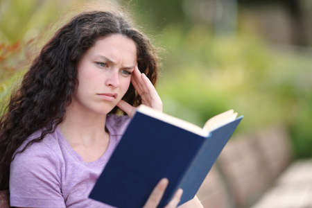 Confused woman reading a bad paper book sitting in a parkの写真素材
