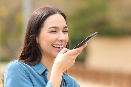 Happy woman dictating message using voice recognition in the street on smart phoneの写真素材