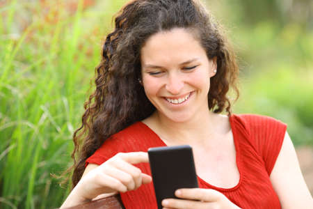 Happy woman in red using smart phone in a parkの写真素材